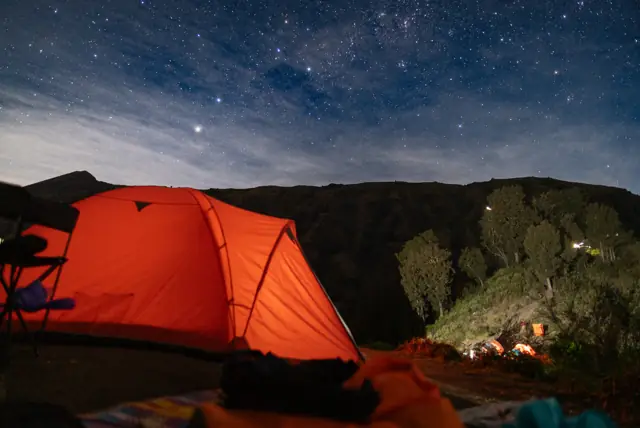 Orange tent under the stars at the crater rim